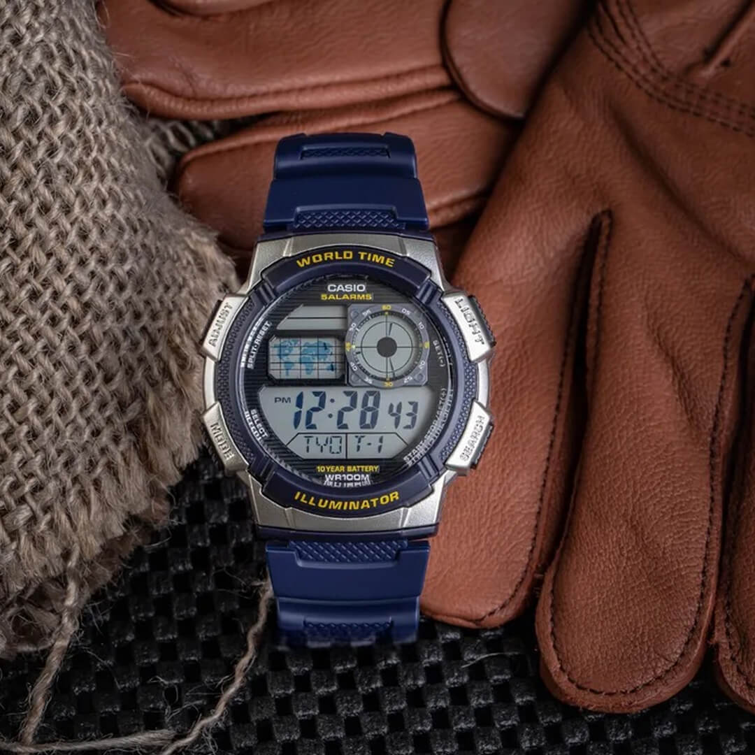 Casio AE-1000W-2AV azul junto a guantes sobre superficie oscura