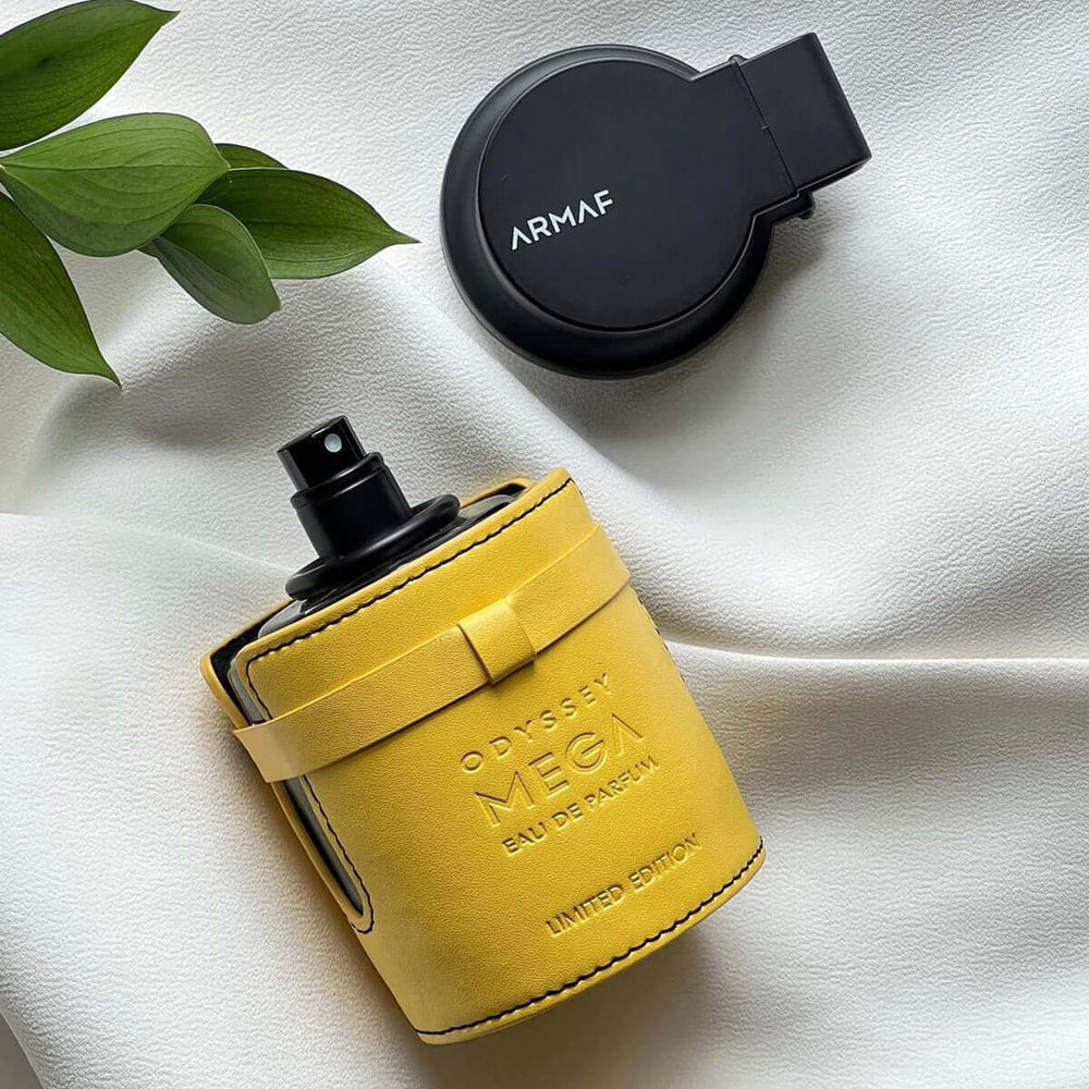 Fragancia Odyssey Mega de Armaf en frasco amarillo, edición limitada, sobre fondo blanco con hojas verdes.